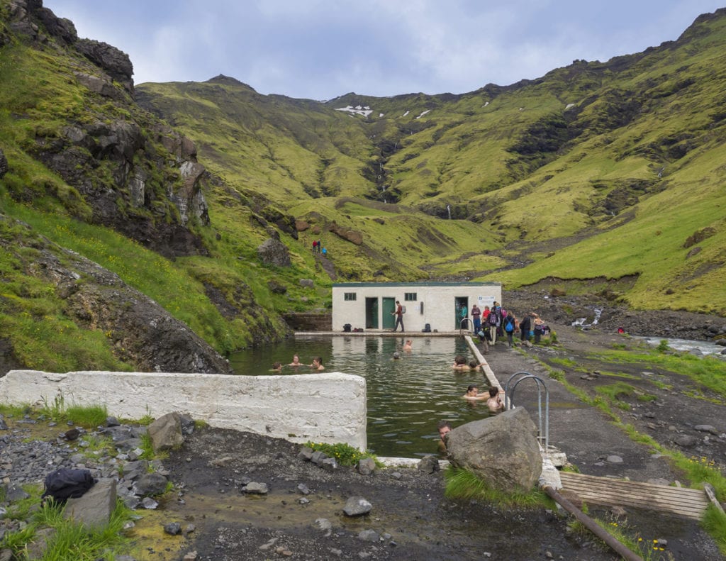 south in Iceland. People swimming and enjoying green warm water in Seljavallalaug secret geothermal pool hiden in valley with green hills, Seljavellir